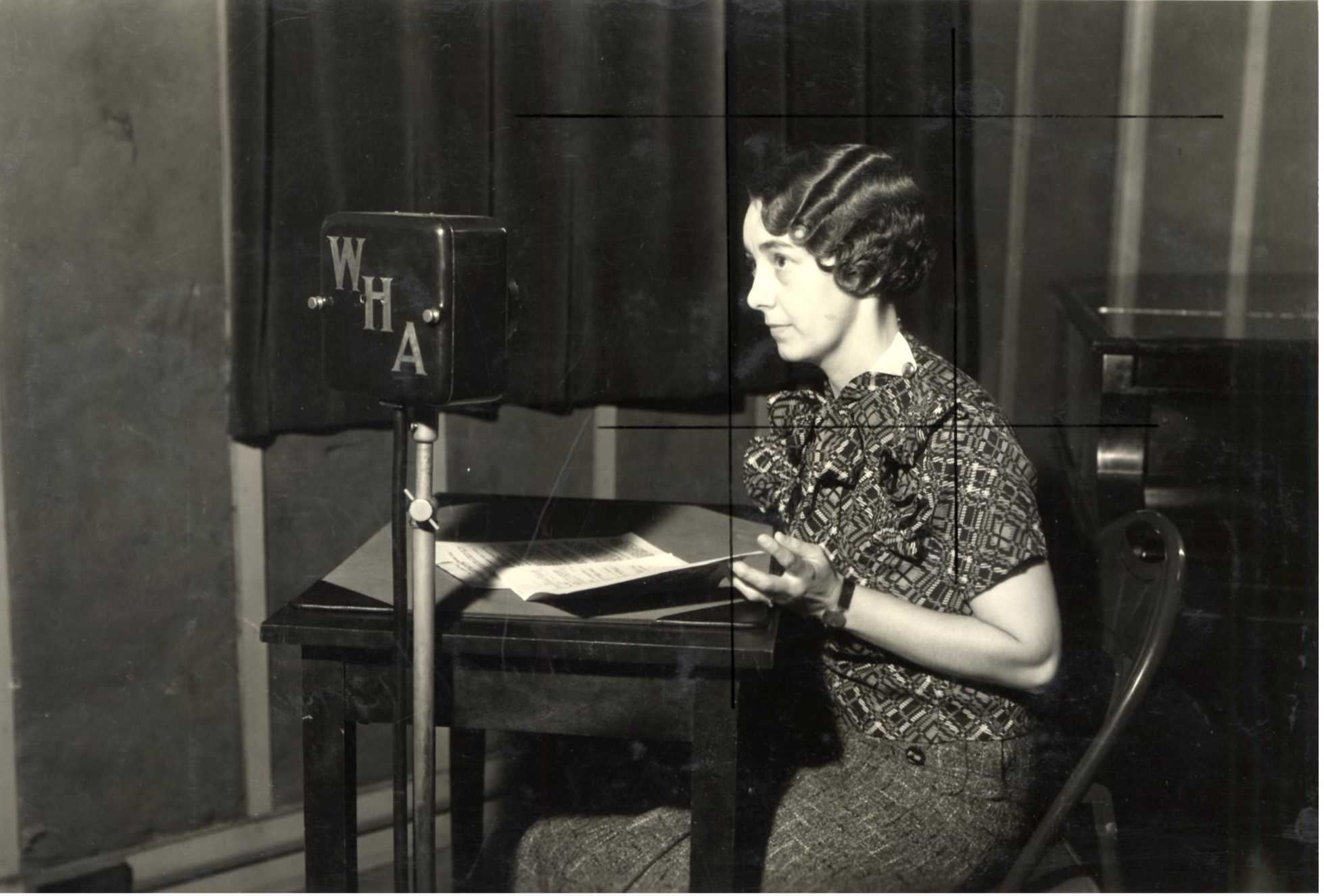 Black and white photo of Aline Hazard at a table with a large microphone labelled WHA.